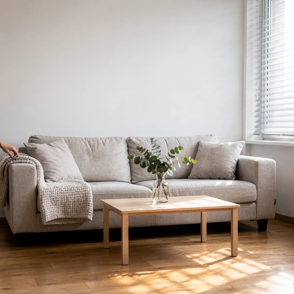 Uprzątnięty salon po home stagingu - jasna kanapa z narzutą, drewniana ława i eukaliptus w wazonie